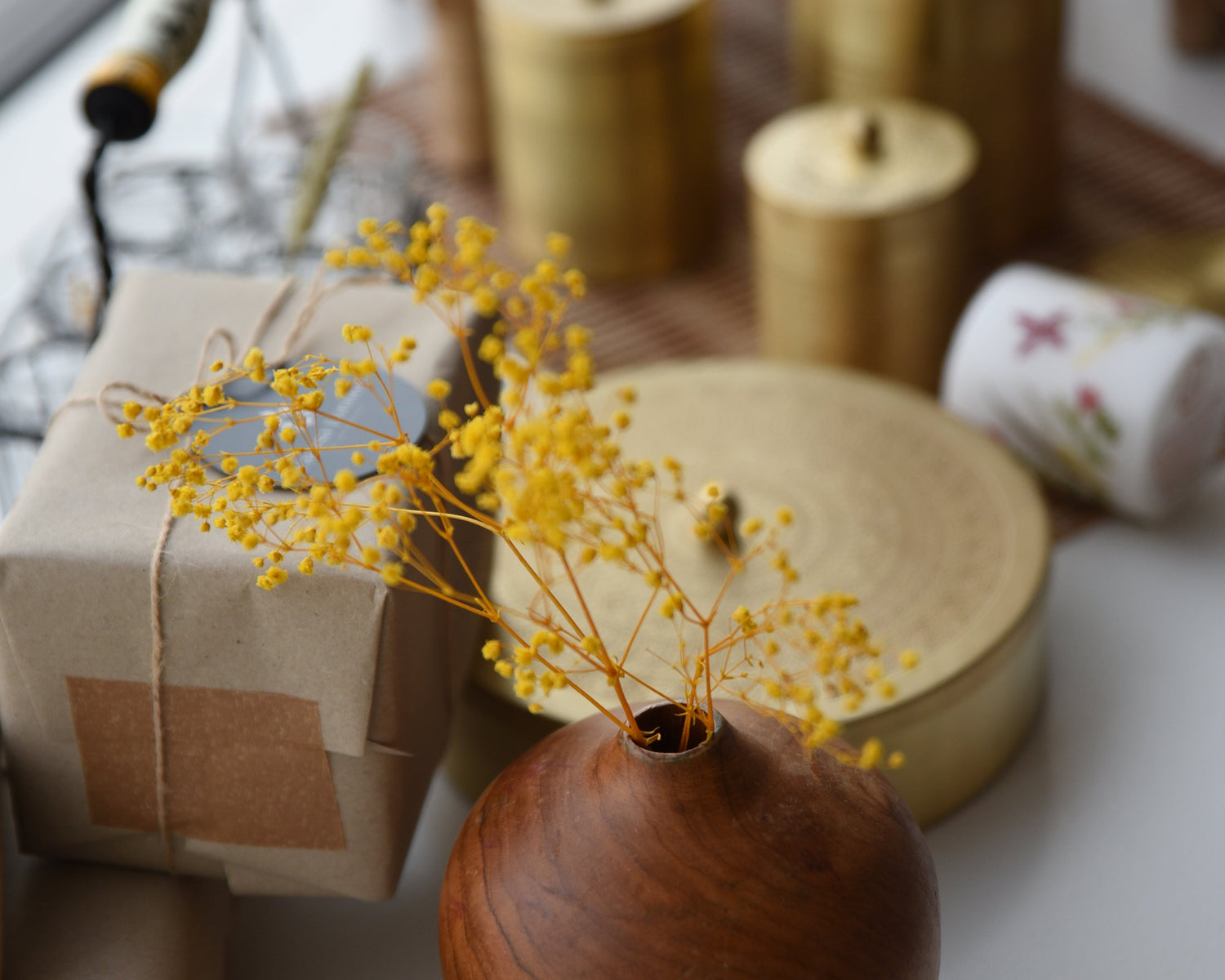 Wooden vase with yellow dried flowers on a white surface with blurred background