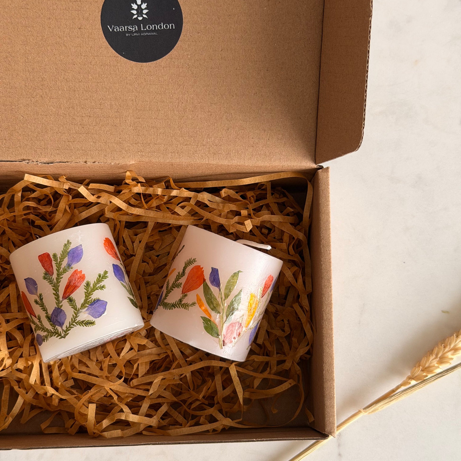 Two decorated candles in a brown box with decorative straw on a light background