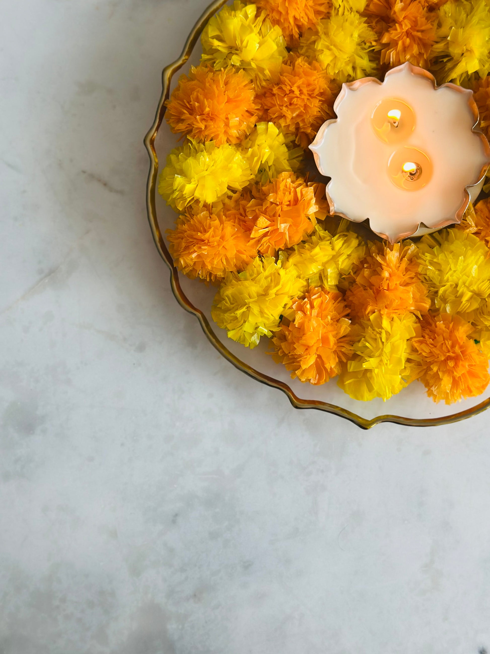 Decorative arrangement of yellow and orange flowers with a lit candle on a marble surface