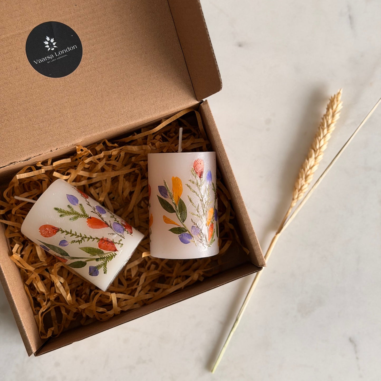 Two decorated candles in a box with a visible brand logo on a light background