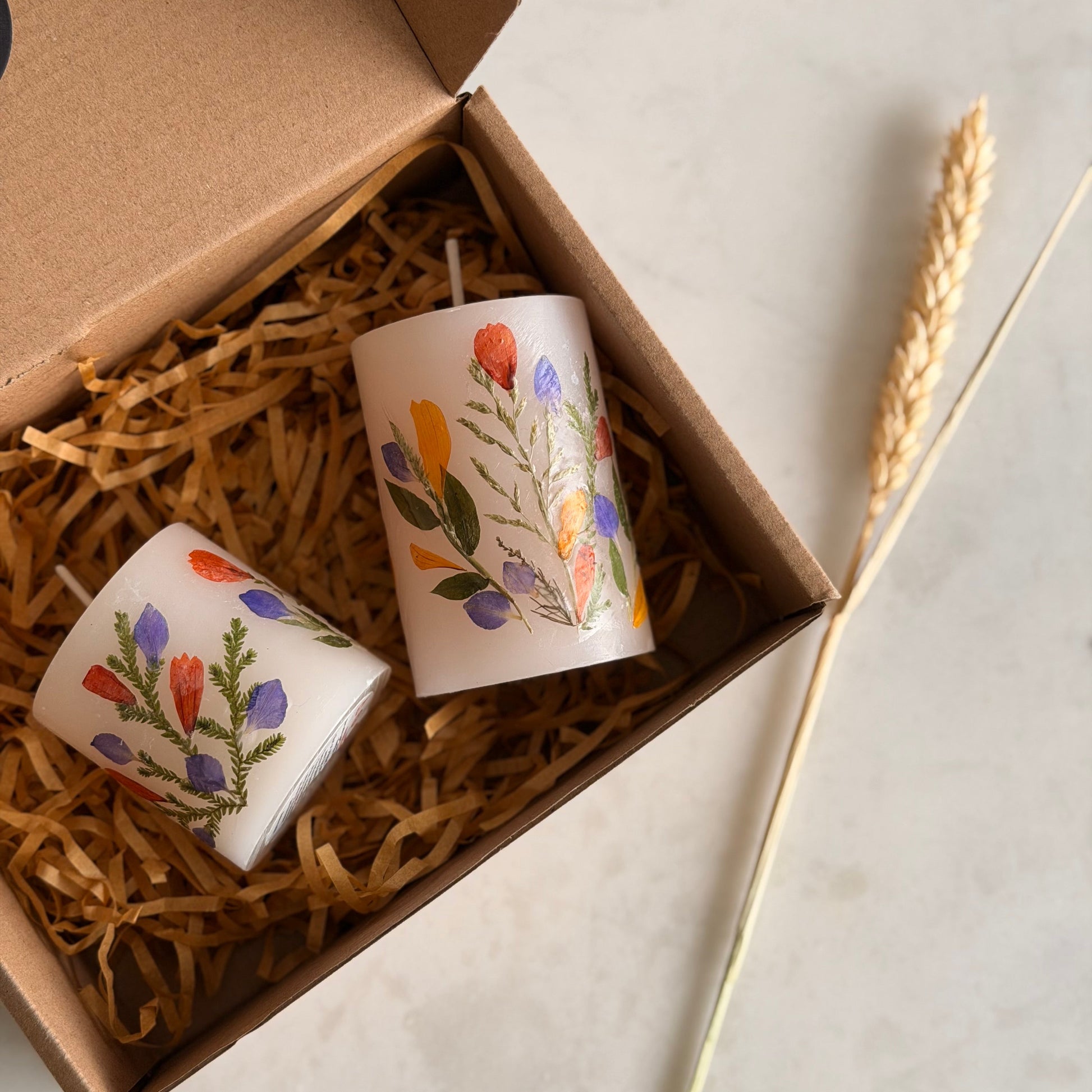 Two decorated candles in a box with straw padding, on a light surface.