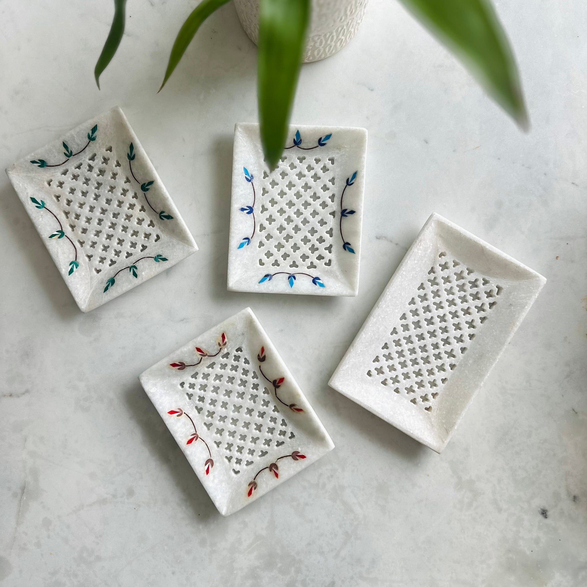 Four small ceramic trays with decorative patterns on a marble surface.