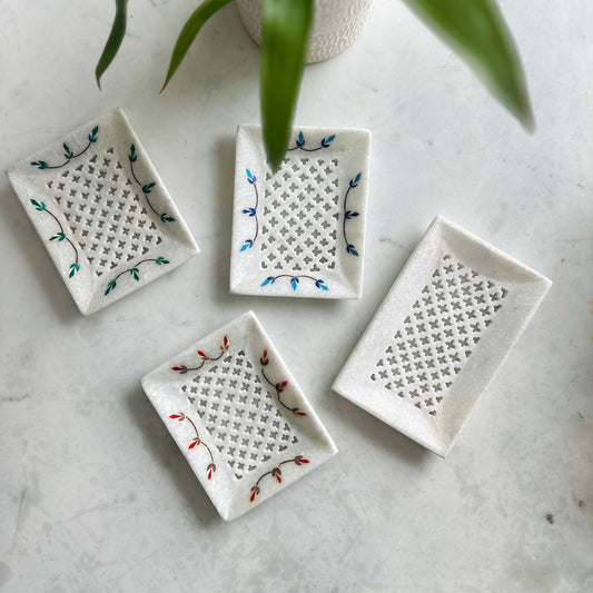 Four small ceramic trays with decorative patterns on a marble surface.
