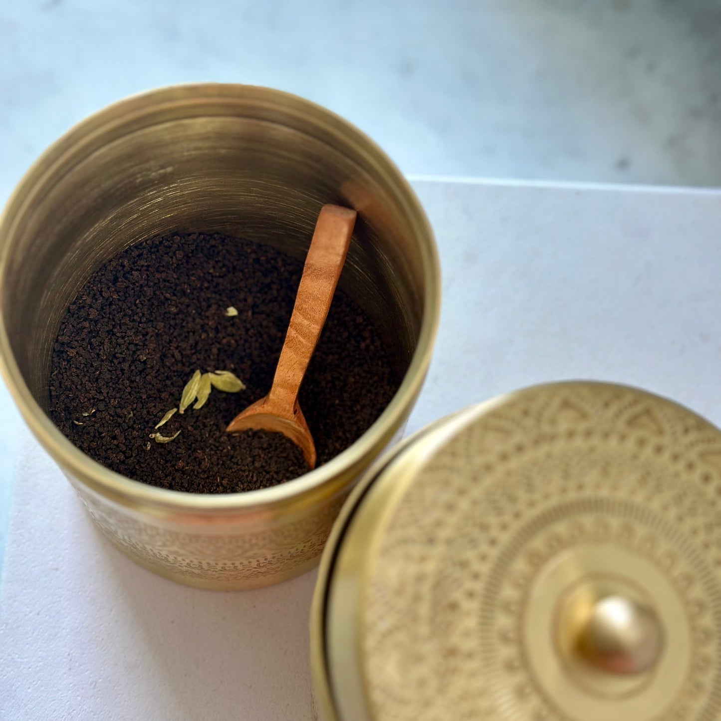 Open brass canister with tea leaves and a wooden scoop