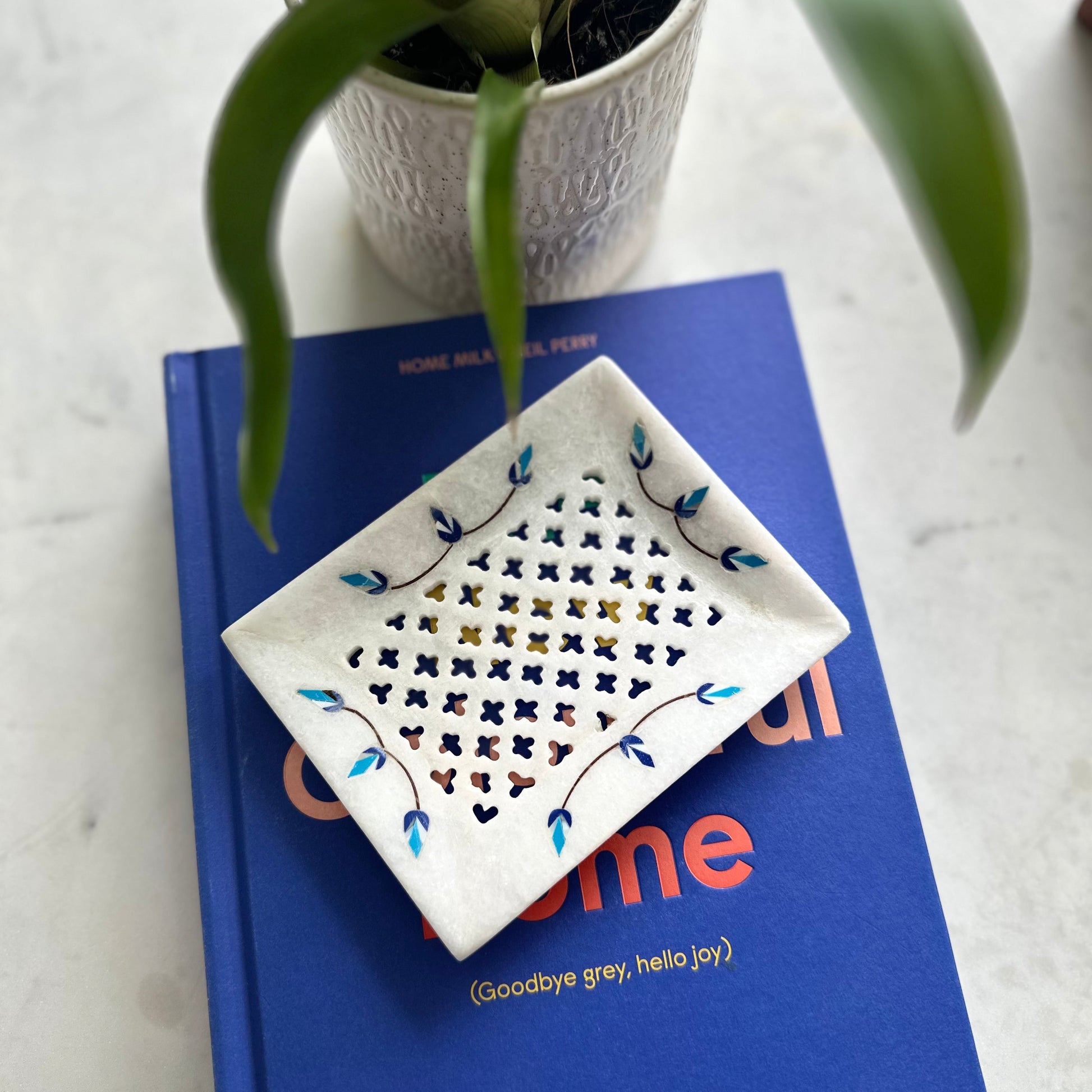 Decorative dish with floral patterns on a blue book with 'Goodbye grey, hello joy' text.