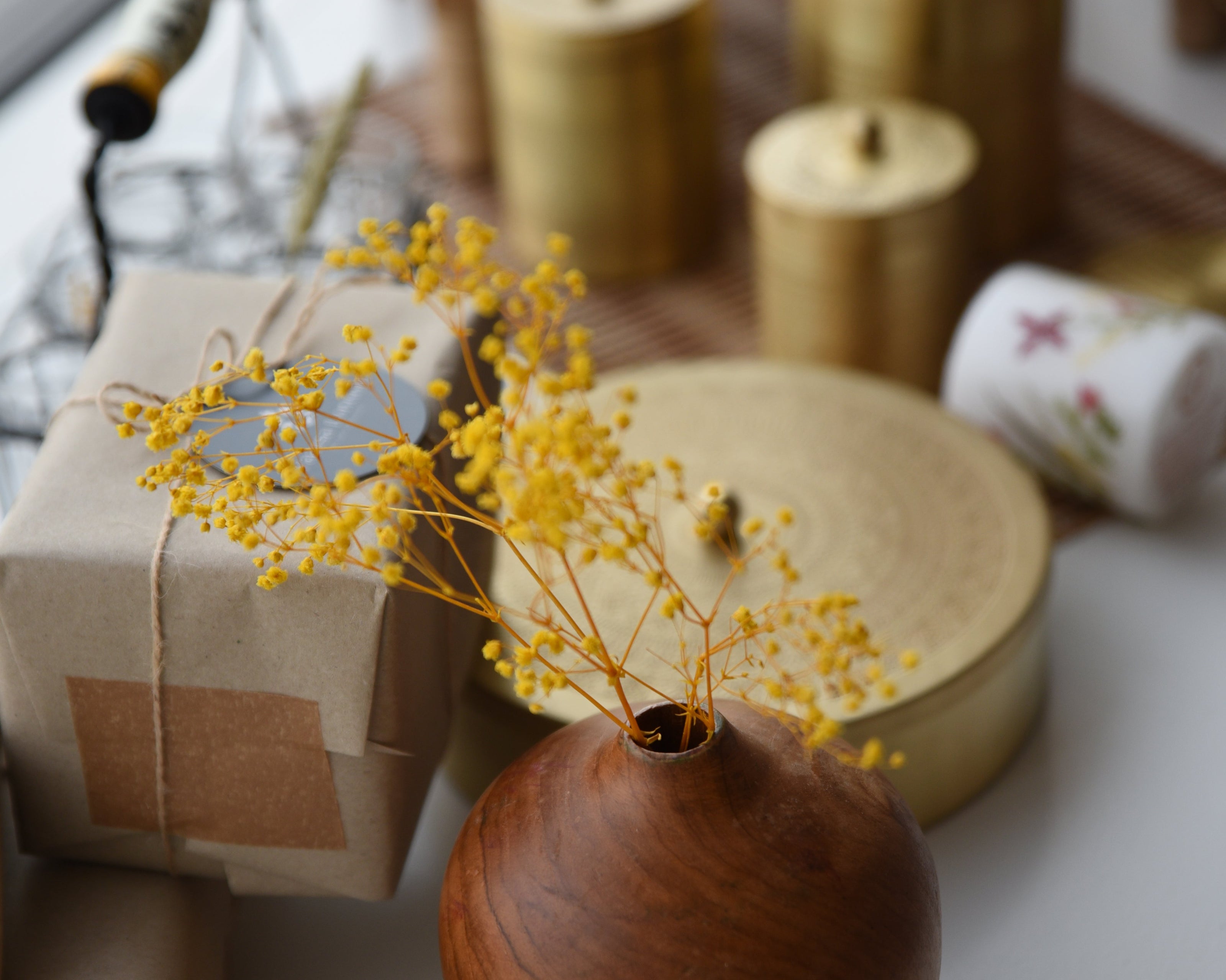 Wooden vase with yellow dried flowers on a white surface with blurred background