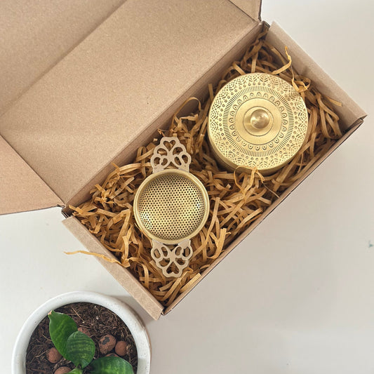 Two brass decorative items in a box with a small plant on a white surface