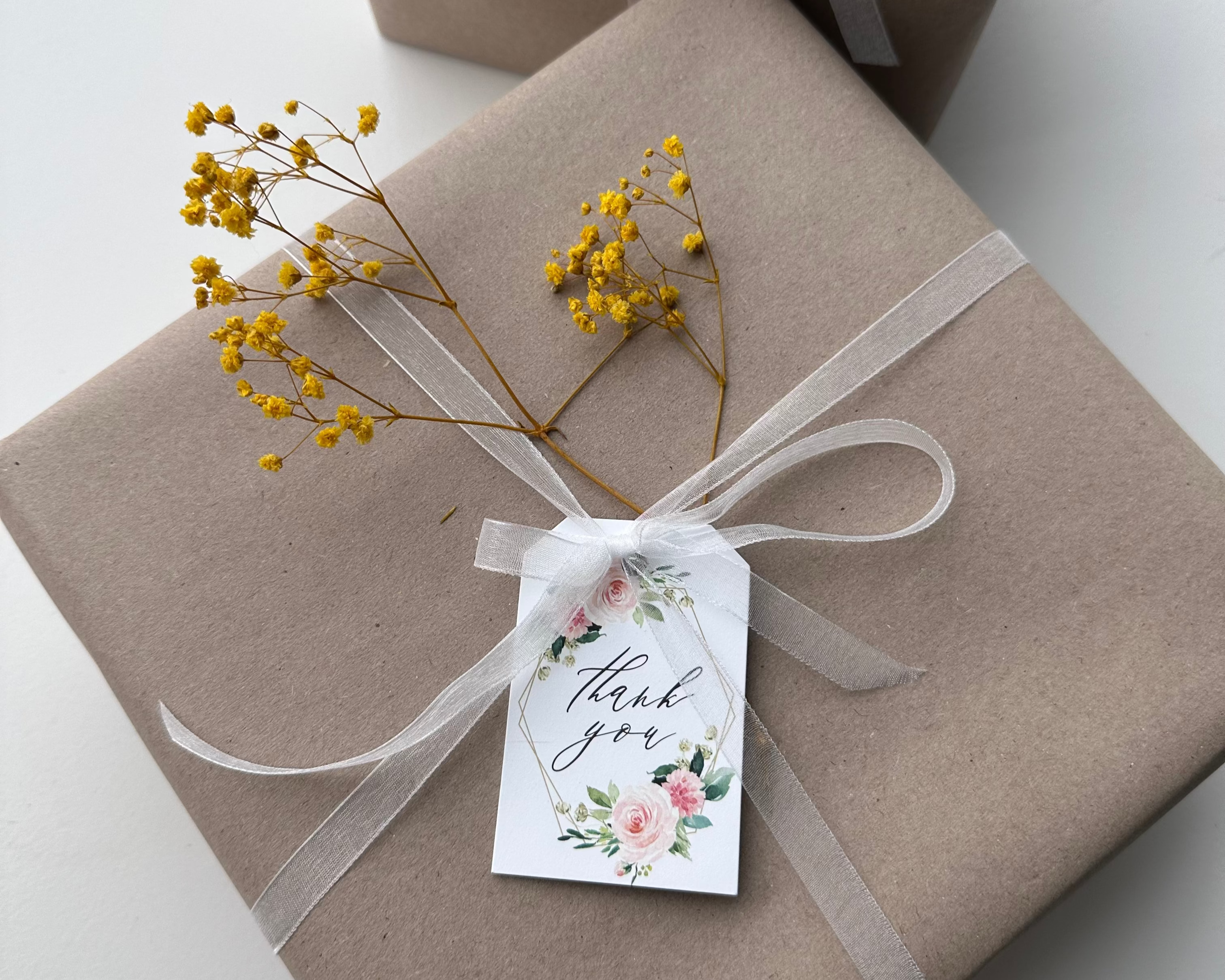 Two wrapped gifts in brown paper with ribbons and 'thank you' tags on a white surface.