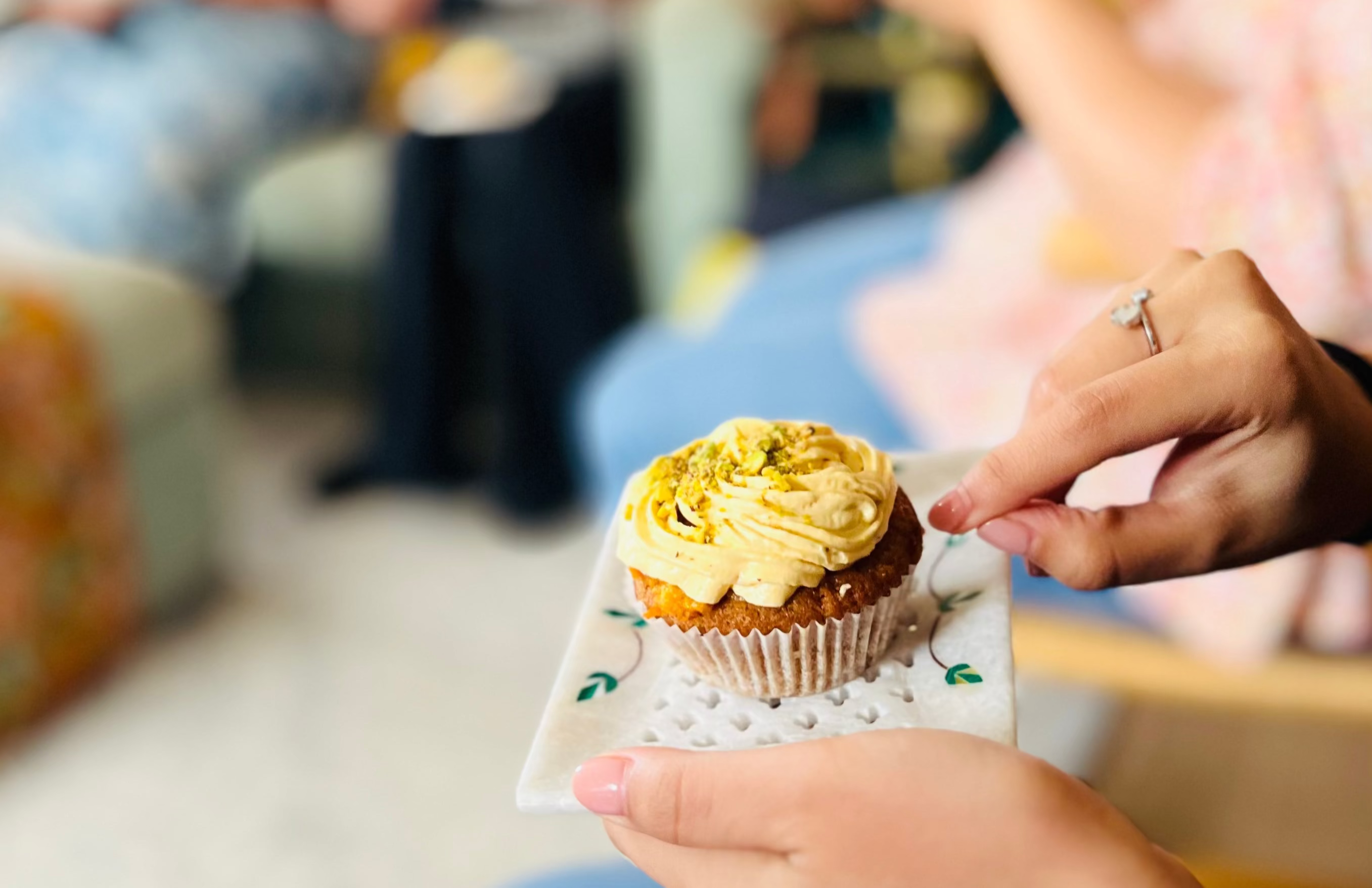 Person holding a cupcake with a blurred background of people sitting on a couch.