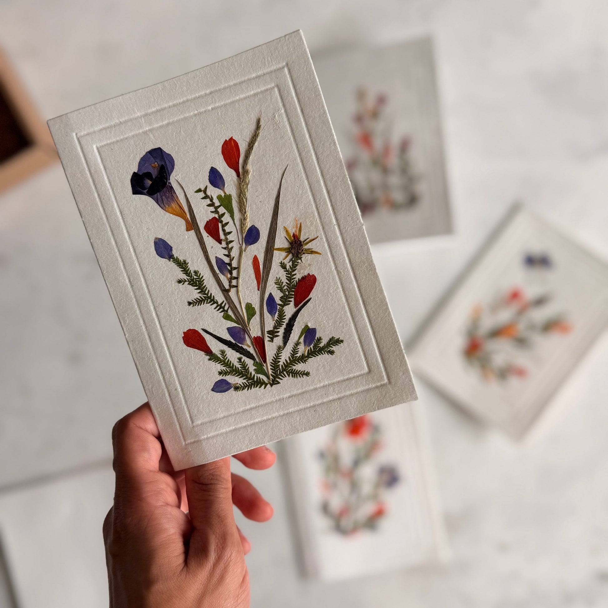Hand holding a card with embroidered floral design against a light background