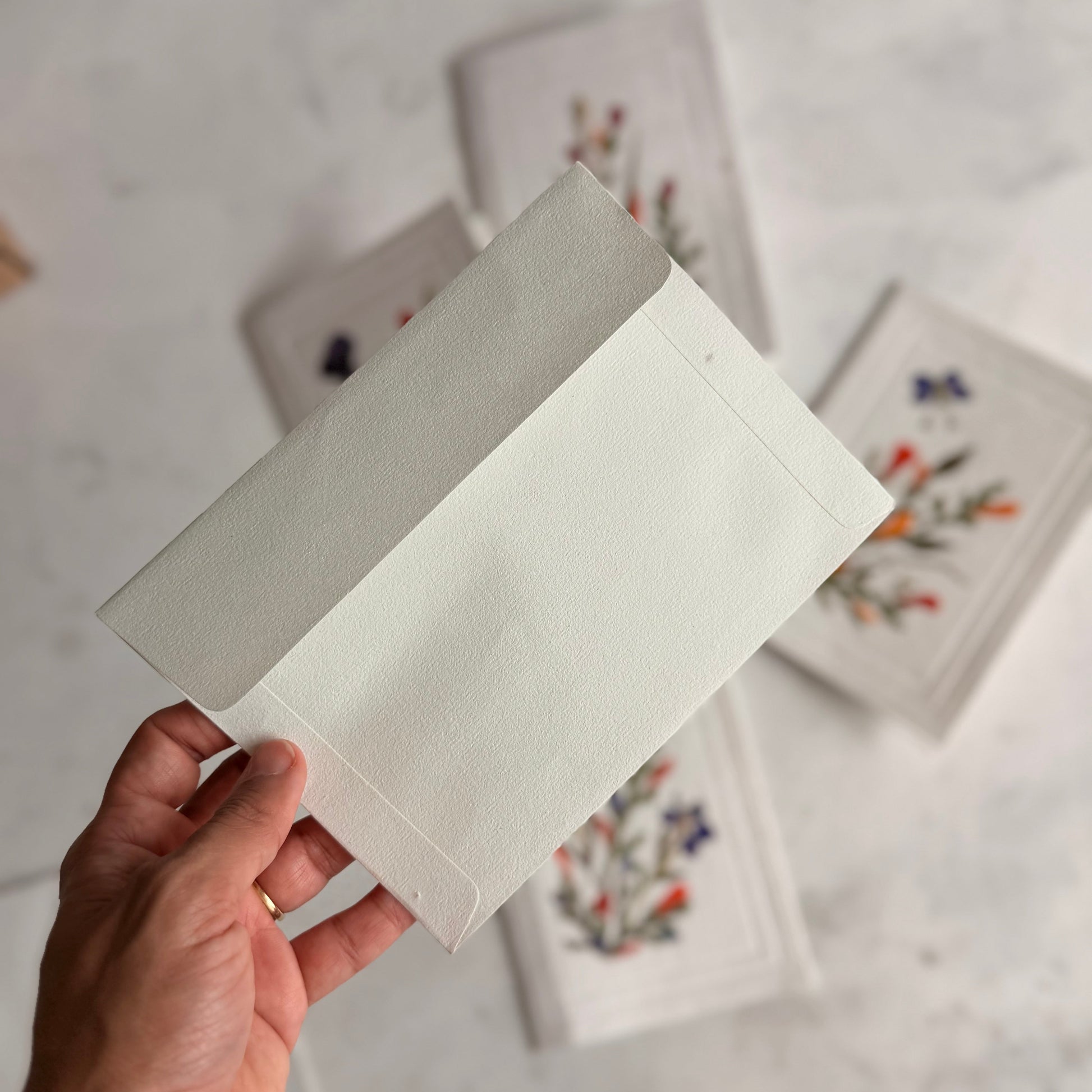 Hand holding a white card with floral designs in the background