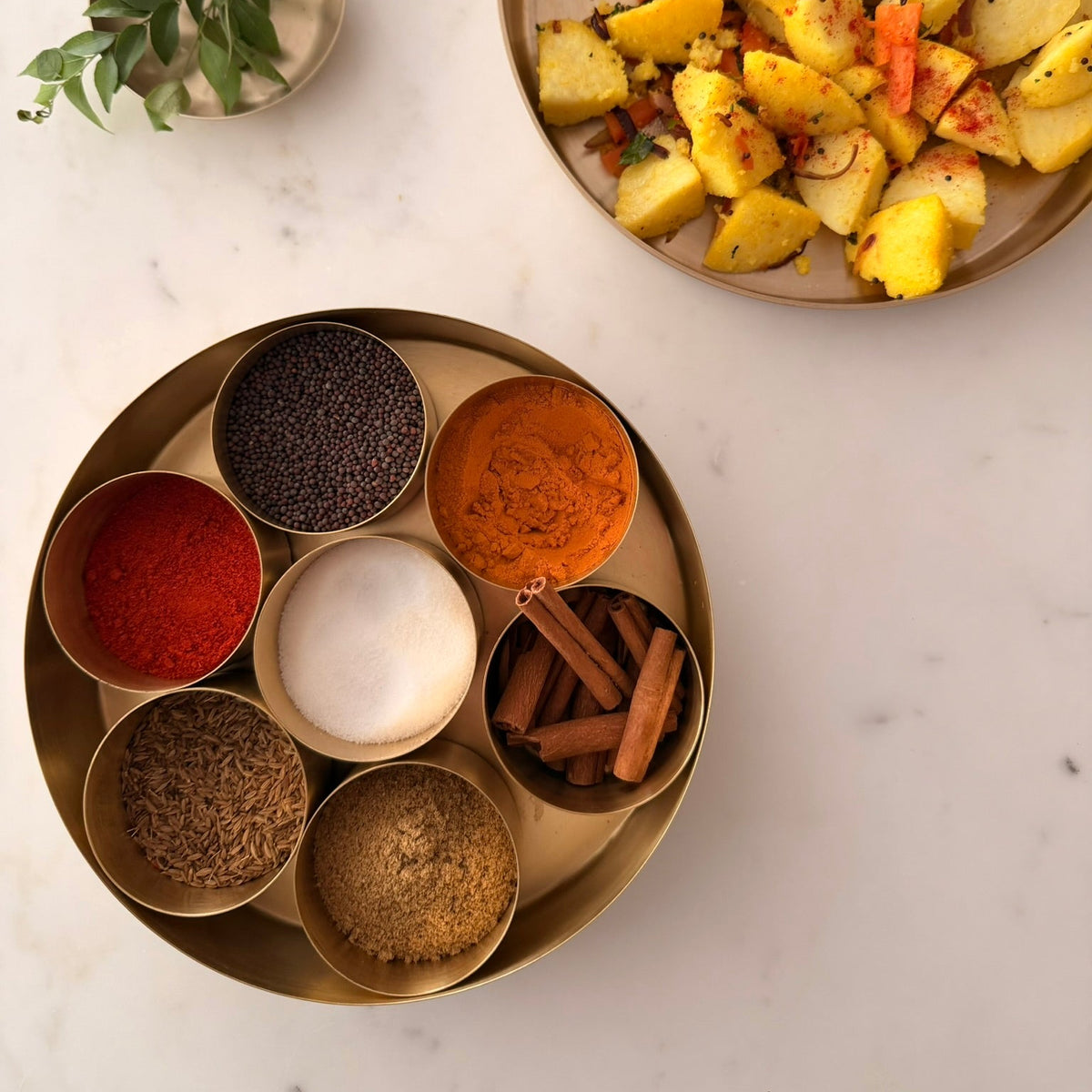 Spice set on a marble surface with a plate of food in the background