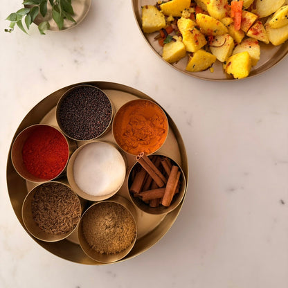 Spice set on a marble surface with a plate of food in the background