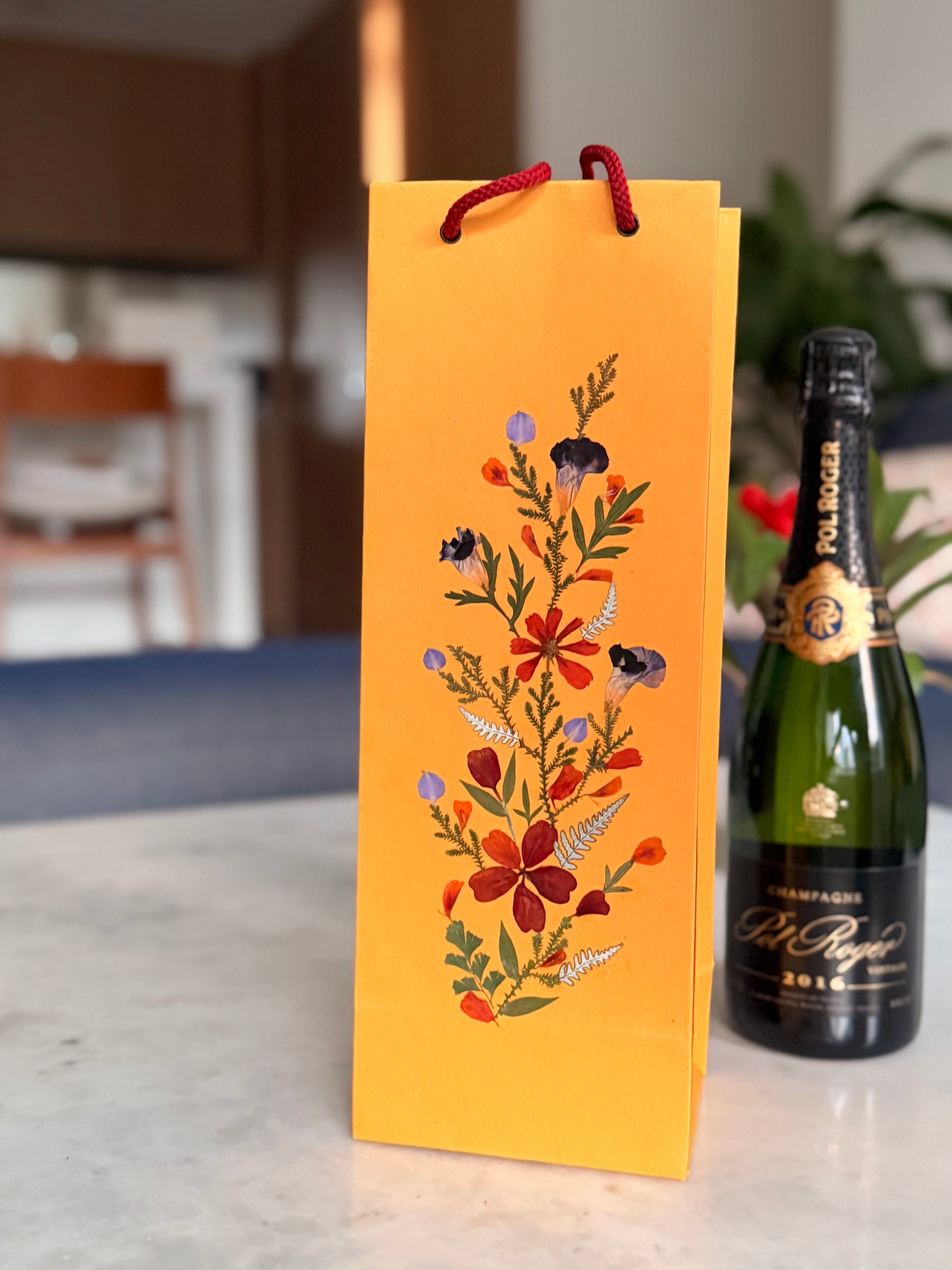 Decorative wine bottle box with floral design next to a champagne bottle on a table.
