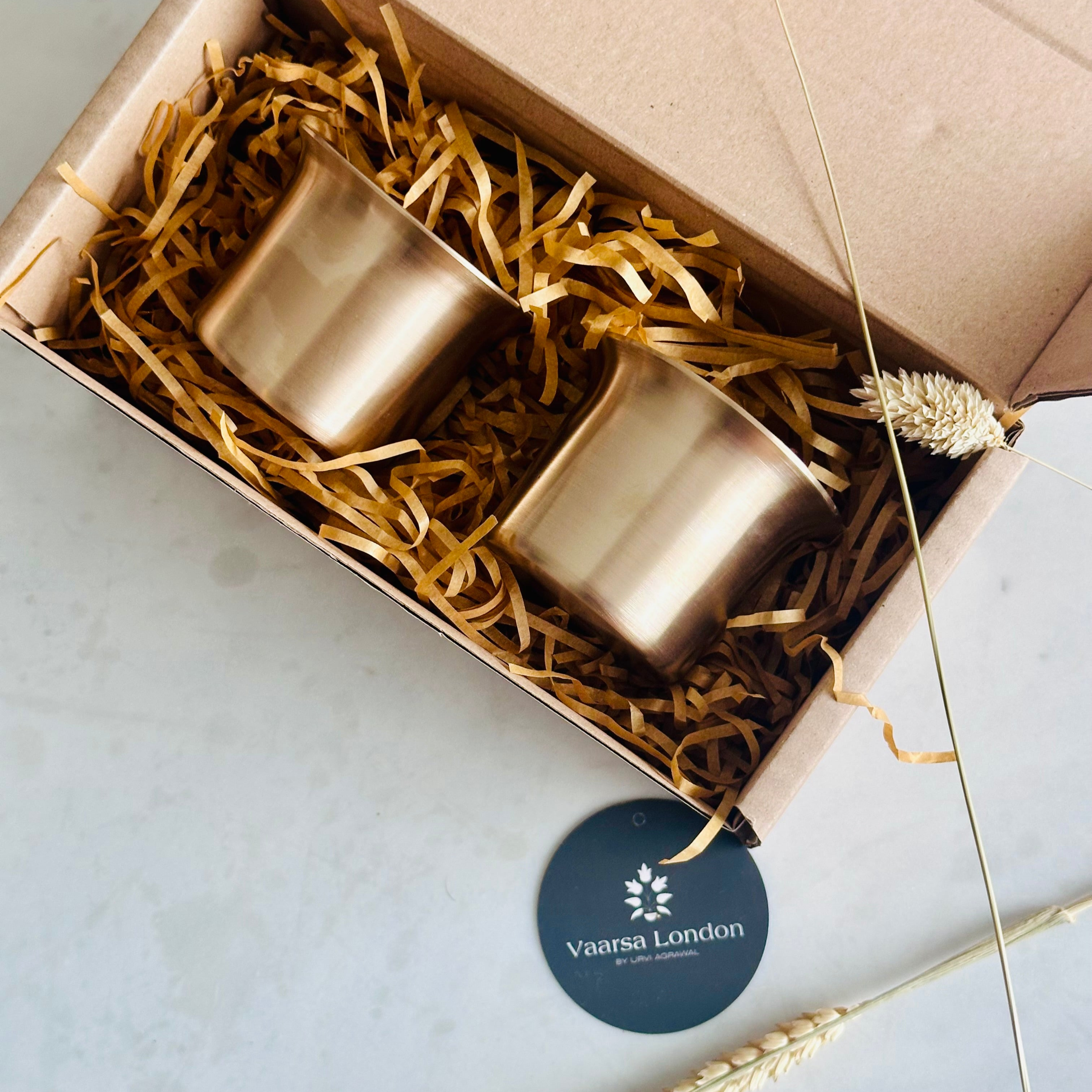 Two gold candle holders in a box with decorative straw and a 'Vamia London' sticker on a light background.