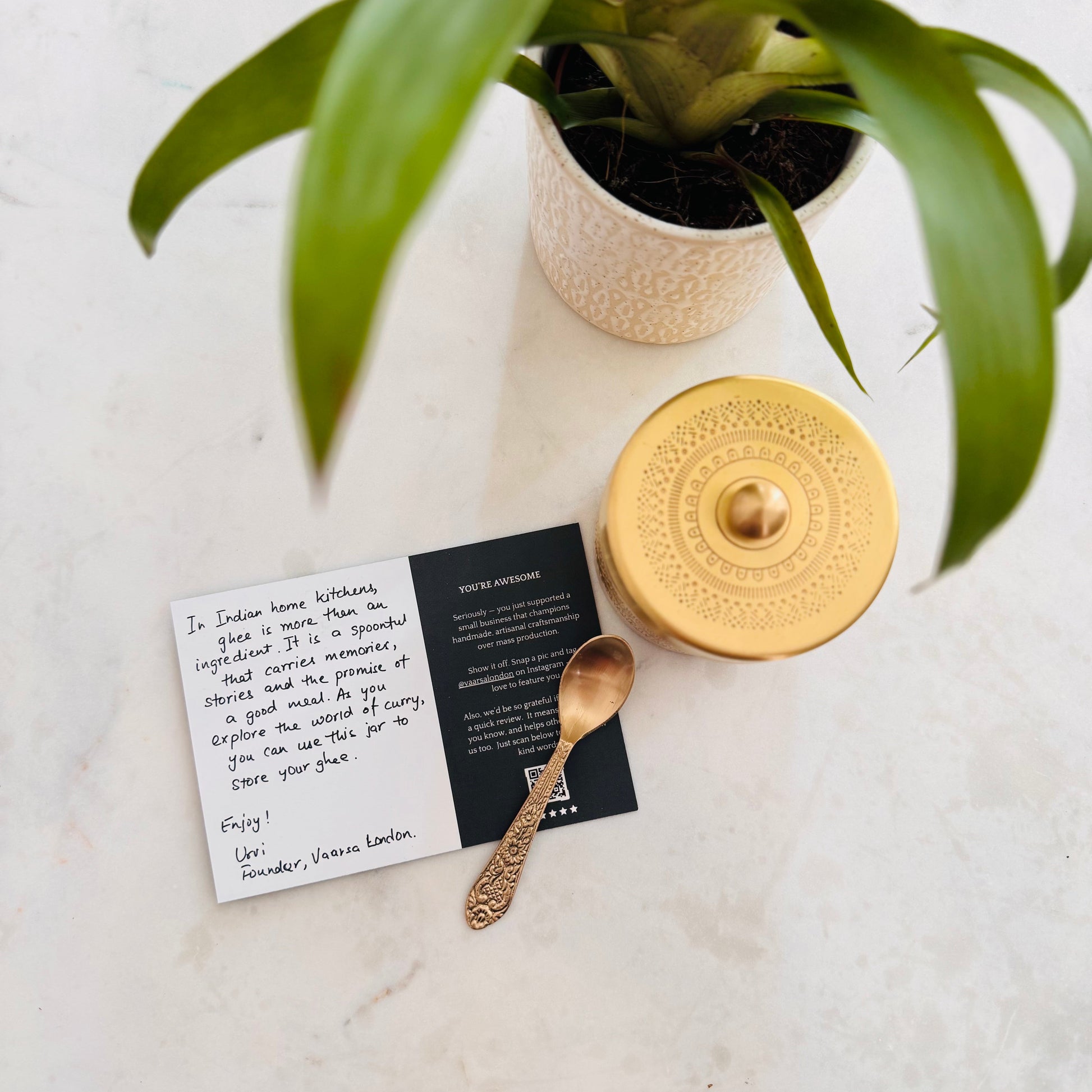 Gold decorative object, spoon, and cards on a marble surface with a plant in the background