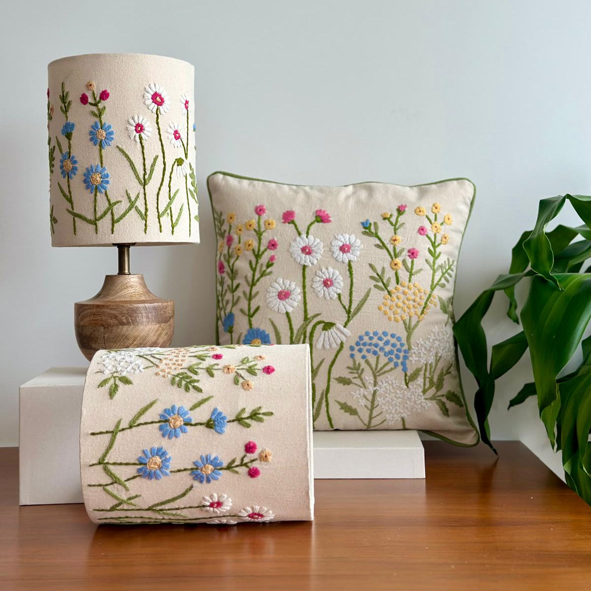 Decorative lamp, pillow, and box with floral embroidery on a wooden surface.