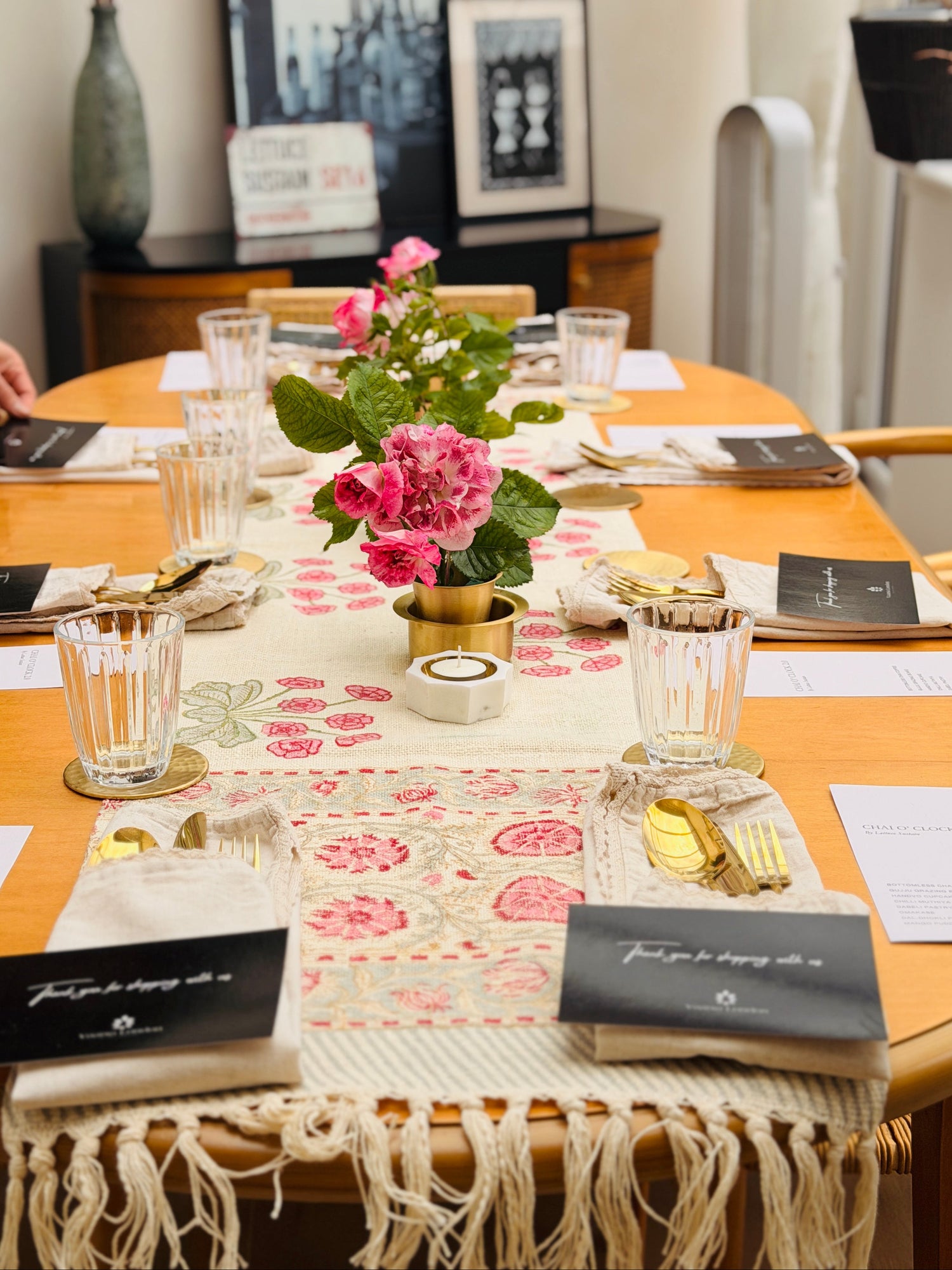 Block-printed table runner, brass coasters and a brass bud vase of pink roses set for a dinner tablescape