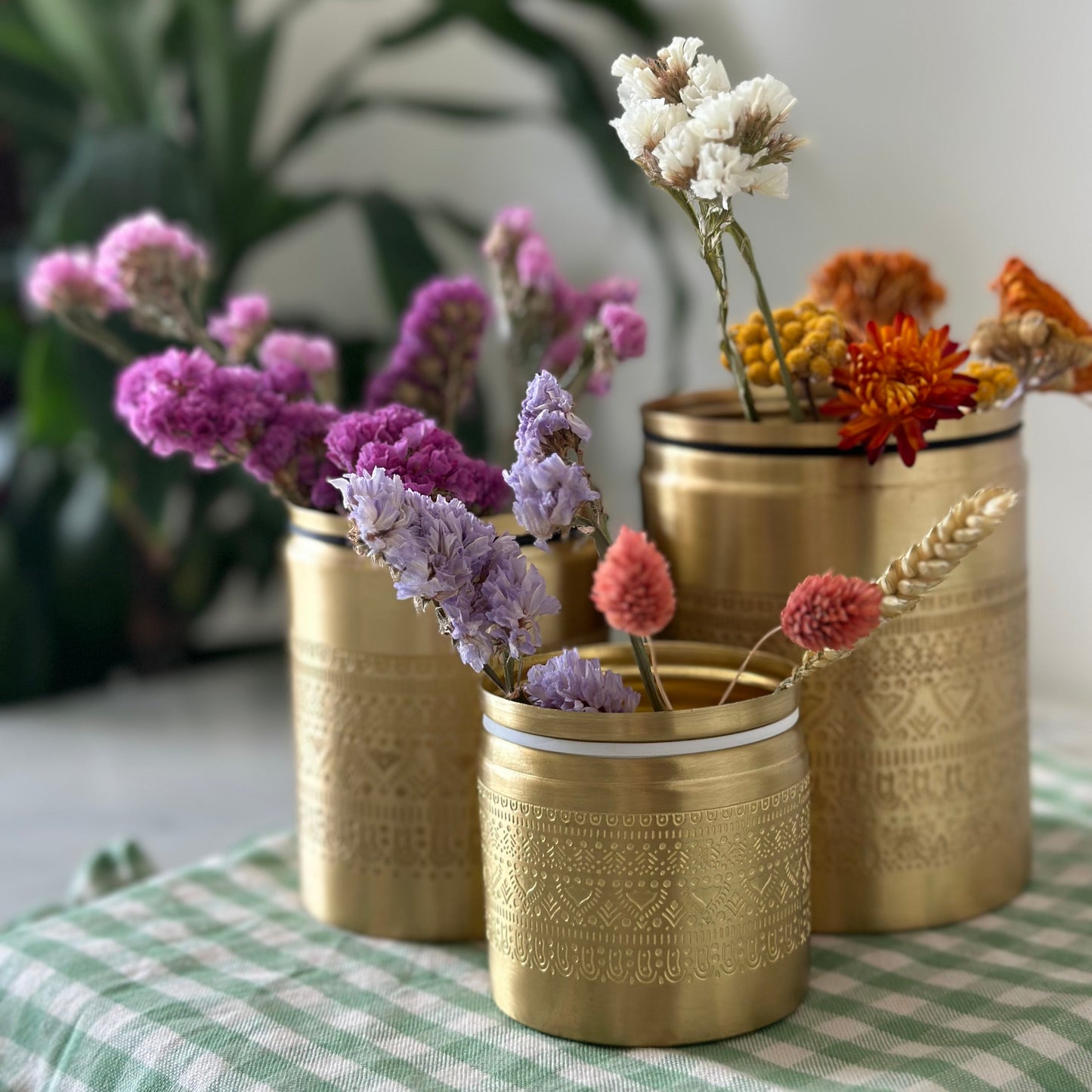 Three brass canisters with floral engraving holding flower stems