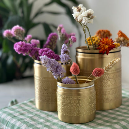 Three brass canisters with floral engraving holding flower stems