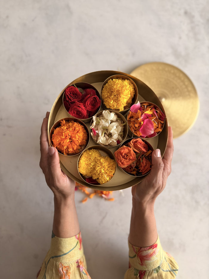 Hands holding a brass spice box filled with marigold, rose and jasmine flowers for a festive table