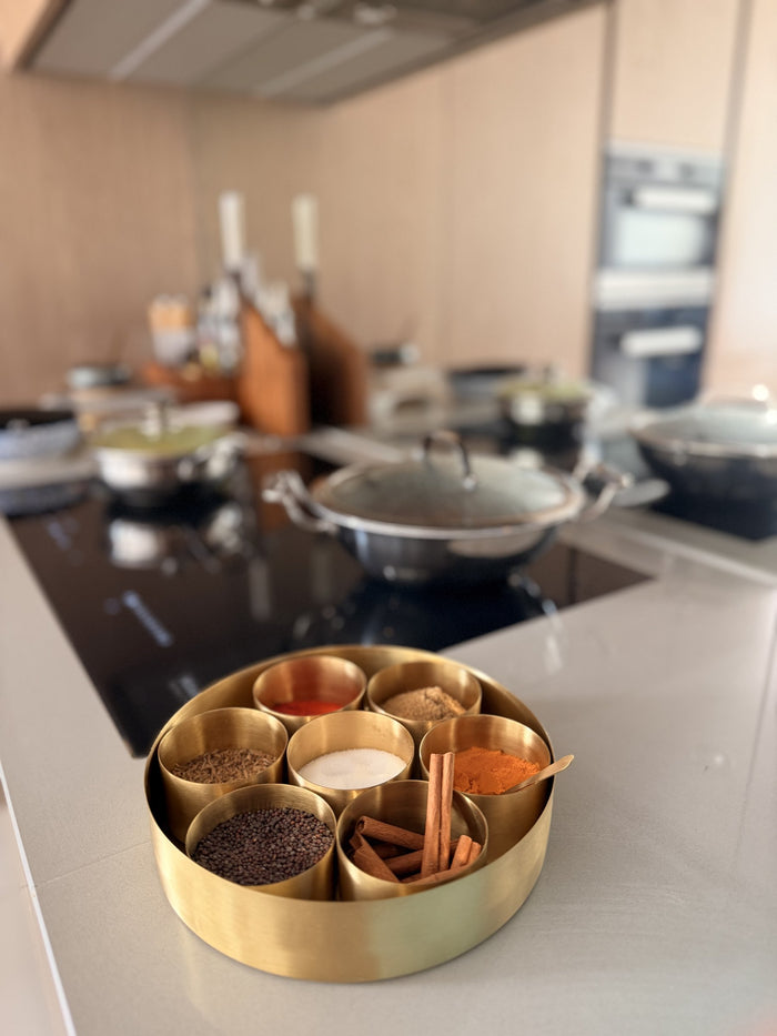 Brass spice box filled with everyday spices on a kitchen counter beside the hob